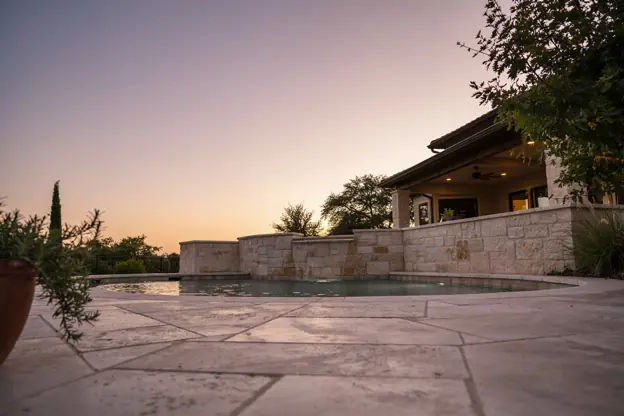 Raised spa spilling into a pool at dusk with a limestone wall